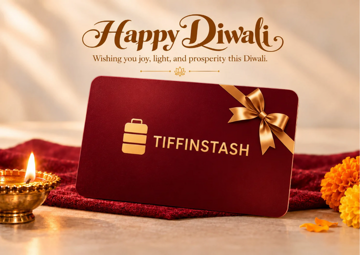 A TiffinStash Diwali Special Gift Card displayed in a festive setting with lit diya lamps, marigold flowers, and traditional Indian decor. The background features a large 'Happy Diwali' greeting in gold lettering on a deep red backdrop.