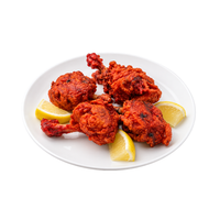 Four pieces of fried chicken coated in a bright red chili-tarare sauce, served on a white plate with lemon wedges on a clean white background.
